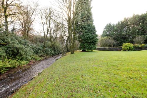 a grassy field with a stream in the middle at Strathendrick House Magnificent property with Garden in Drymen