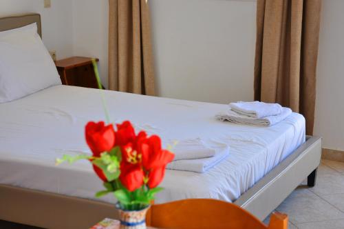 a bed with a vase of red flowers and towels at Lagos Studios & Apartments in Palekastron