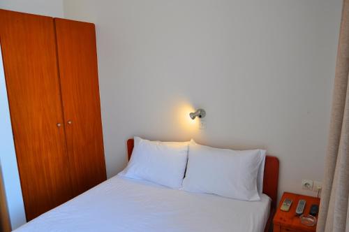 a bed with white sheets and a light on the wall at Nora Hotel in Sitia