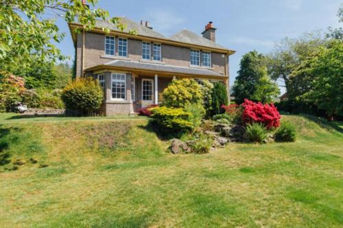 a large house on a grassy hill with bushes at Newholme House in Stirling
