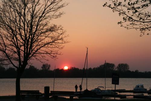 una puesta de sol sobre el agua con dos personas de pie cerca de un muelle en Schlafwagen Beachvolleyball, en Xanten