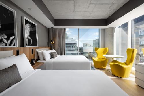 a hotel room with two beds and yellow chairs at Humaniti Hotel Montreal, Autograph Collection in Montréal