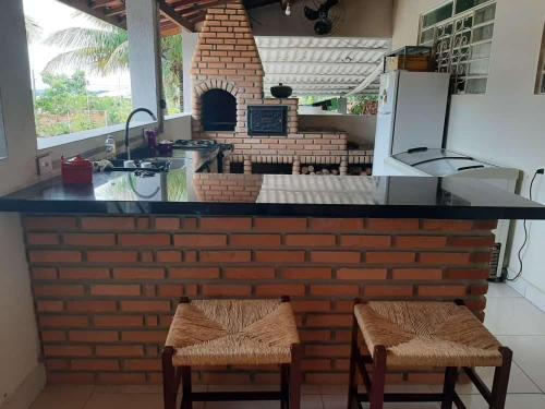 a kitchen with a counter and two stools in front of a brick oven at Chacara Oliva in Piracicaba