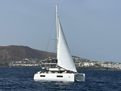 a white sailboat in the water with a city in the background at Catamaran White Beach in Playa Blanca