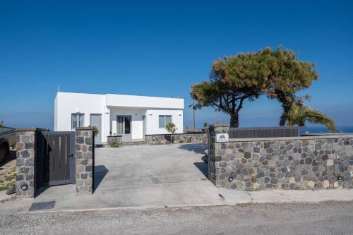 a white house with a stone fence and a tree at Bliss Holidays Spot in Fira