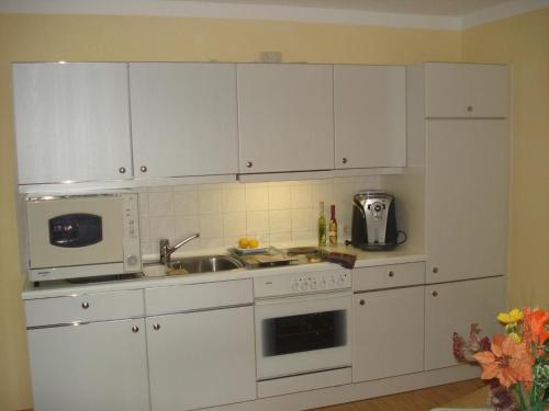 cocina con armarios blancos, fregadero y microondas en Appartement in Hönigsgrub mit Großem Balkon und Fernblick en Rinchnach