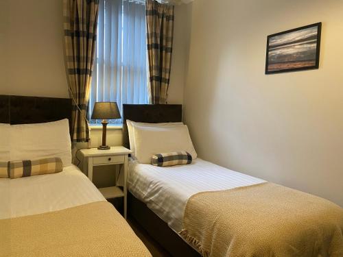 a bedroom with two beds and a lamp and a window at Brampton Holiday Homes - Beckside Apartment in Brampton