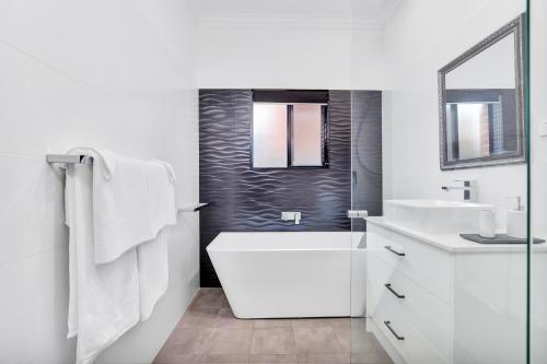 a white bathroom with a tub and a sink at Noir Cottage Glenelg North in Glenelg