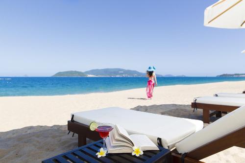 a woman standing on a beach with a bed and a book at Regalia Nha Trang in Nha Trang