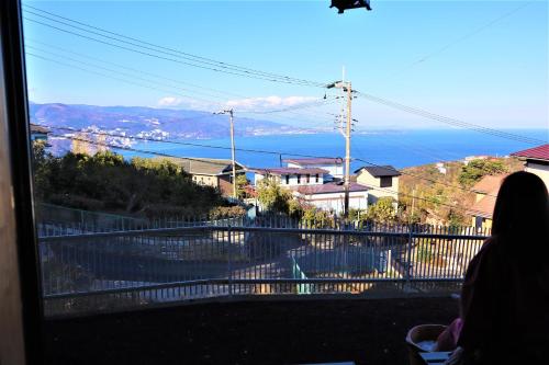 a woman looking out of a window at the ocean at 熱海の海が一望できる温泉付貸別荘 満月あじろ mitsukiajiro in Atami