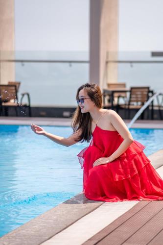 a woman in a red dress sitting next to a swimming pool at Diamond Sea Hotel in Da Nang