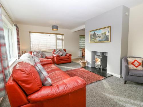a living room with a red leather couch and a fireplace at Cae Glas in Pwllheli