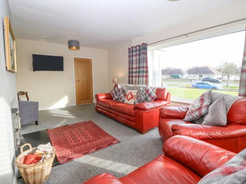 a living room with red leather furniture and a large window at Cae Glas in Pwllheli