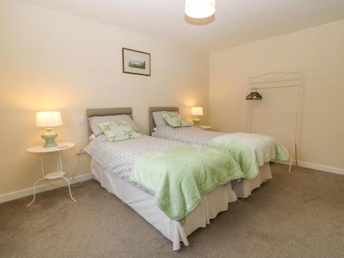 two beds in a bedroom with a table and lamps at Cae Glas in Pwllheli