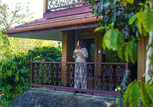 a woman standing on a balcony talking on a cell phone at Niyatma Wayanad Pool Resort by VOYE HOMES in Wayanad