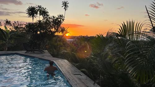 a man in a swimming pool with the sunset in the background at La Petite Kaz Dans la Savane in Fleurimont