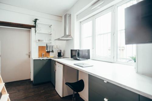 une cuisine avec un comptoir blanc et quelques fenêtres dans l'établissement Blue Appart ( studio proche gare Montauban ), à Montauban