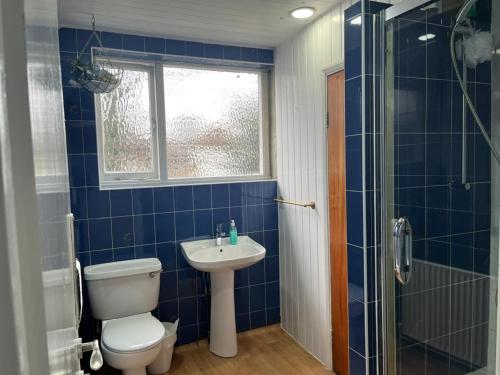 a blue tiled bathroom with a toilet and a sink at Saji Hotel Illford in Ilford