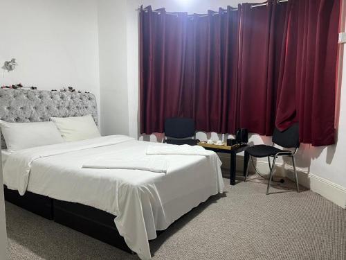 a bedroom with a large bed and red curtains at Saji Hotel Illford in Ilford