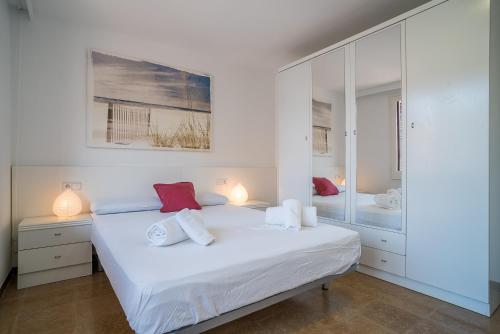 a white bedroom with a bed and a mirror at Canet beach 3 in Canet de Mar