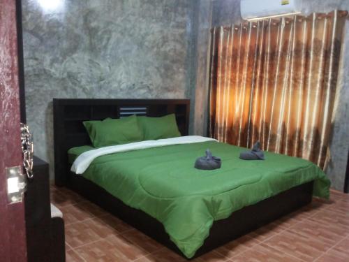 a bedroom with a green bed with two black shoes on it at Bansappoori in Lamphun
