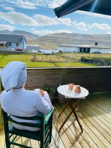 a person sitting in a chair on a deck with a table at Nice one-story house in Suduroy in Tvøroyri