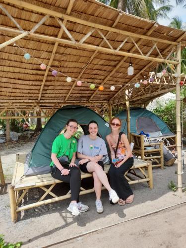 three people sitting on a bench under a tent at Ganja Gardens Camping in Ban Nua