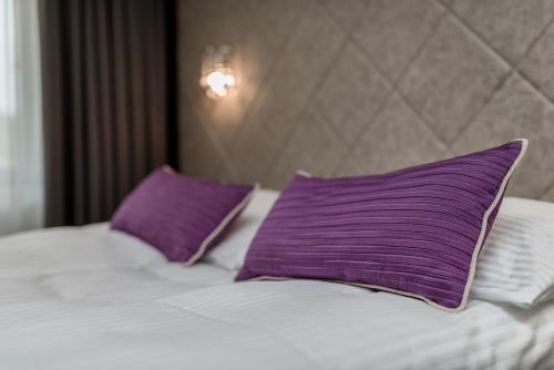 a bed with purple and white pillows on it at Evita Hotel & SPA in Tleń