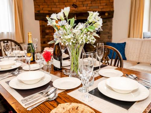 a table with white plates and a vase of flowers at Pass the Keys Malt House With Hot Tub Stunning Tudor Cottage in Craven Arms