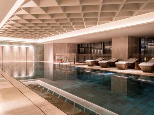 uma piscina num hotel com cadeiras e uma mesa em Sofitel Haikou em Haikou