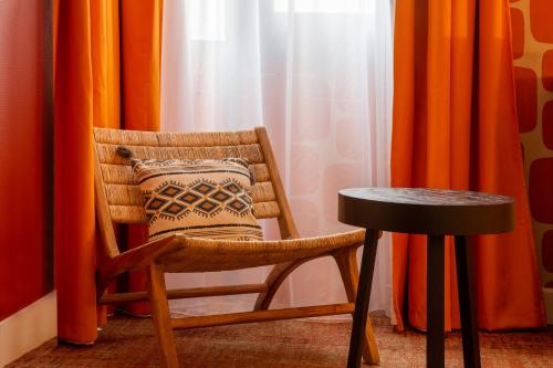 a chair and a table in a room with orange curtains at Aiden by Best Western Paris Roissy CDG in Roissy-en-France
