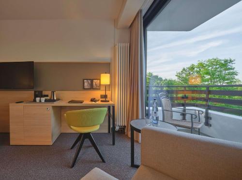 ein Hotelzimmer mit einem Schreibtisch und einem großen Fenster in der Unterkunft Dorint Hotel & Sportresort Arnsberg/Sauerland in Neheim-Hüsten