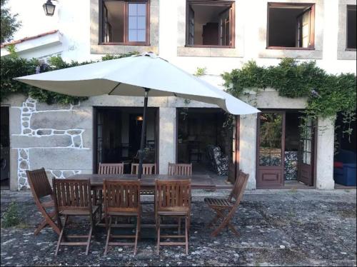 a table with chairs and an umbrella in front of a building at Casa de São Cristóvão - 4r and private swimmingpool in Vila de Punhe