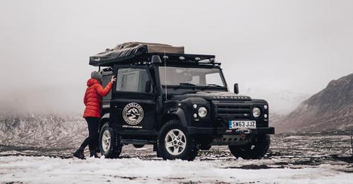 uma pessoa ao lado de um jipe preto na neve em Land Rover Defender Luxury Camper em Morpeth