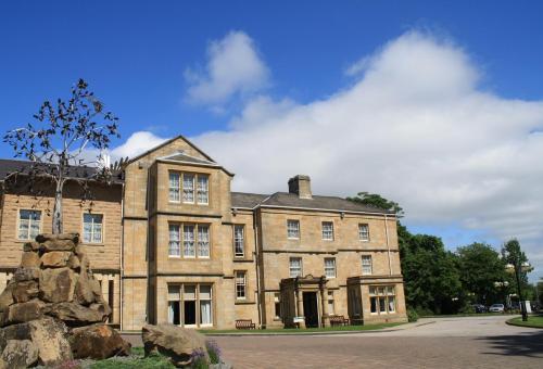 un grand bâtiment en briques avec un arbre devant lui dans l'établissement Weetwood Hall Estate, à Leeds
