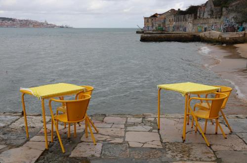 two yellow tables and chairs sitting next to the water at Casa Terra Cota - Almada in Almada