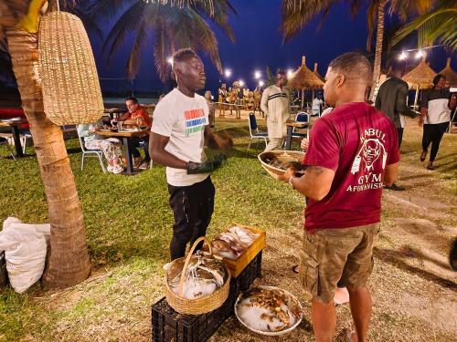 two men standing next to a table with baskets of food at Tamala Beach Resort in Kotu