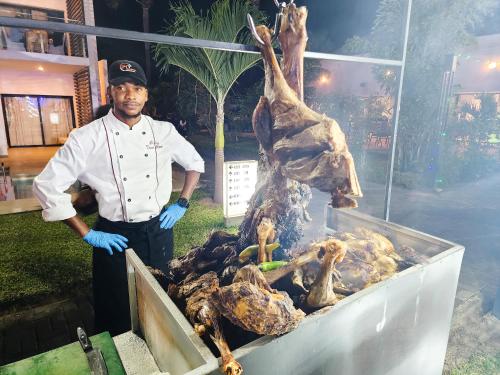a man standing next to a grill with meat at Tamala Beach Resort in Kotu