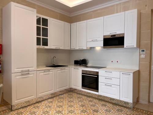 a white kitchen with white cabinets and appliances at Typical Maltese Maisonette in St.Julians in St. Julianʼs