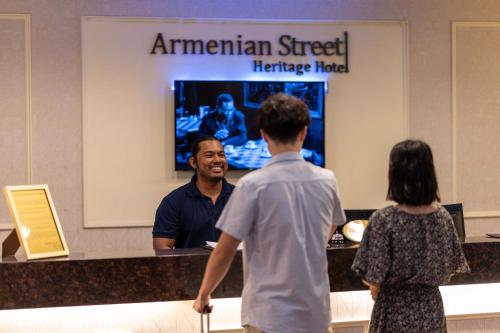 Ein Mann, der vor einer Theke mit einer Frau spricht. in der Unterkunft Armenian Street Heritage Hotel in George Town