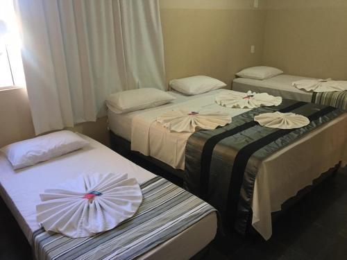 three beds in a hotel room with flowers on them at Klinn Hotel in Tanabi
