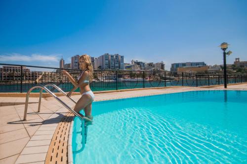 Eine Frau im Bikini, die auf einem Fahrrad im Schwimmbad steht. in der Unterkunft Marina Hotel Corinthia Beach Resort Malta in St Julian's