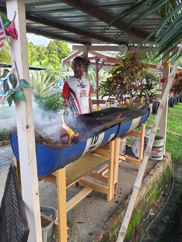 a man cooking food in a boat on a grill at Tmn Rekreasi Cikgu Haron in Labis