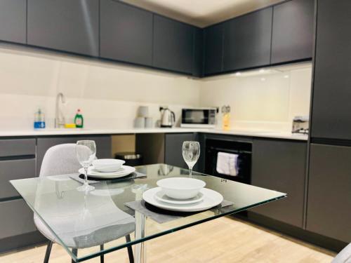 een keuken met een glazen tafel met 2 borden en wijnglazen bij Brand new modern 1 bed apartment near Old Trafford Stadium in Manchester