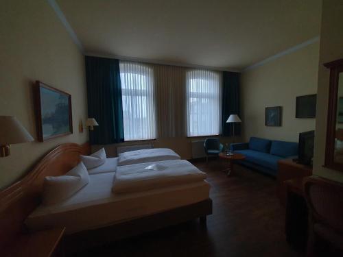 a hotel room with two beds and a blue couch at Hotel Fürstenhof in Rathenow