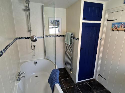 a bathroom with a tub and a shower with a blue door at Longtail Cottage in Sidmouth