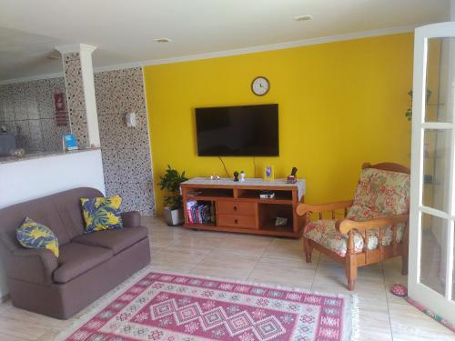 uma sala de estar com um sofá e uma televisão numa parede amarela em Hostel Unamar em Cabo Frio