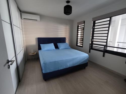 a bedroom with a blue bed and two windows at Charmant F2 à SkyNui, piscine de 25m et vue mer in Papeete