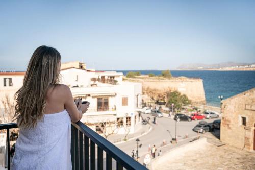 Una mujer parada en un balcón con vistas al océano en Ethos Suites en La Canea