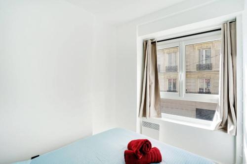 - une serviette rouge assise sur un lit devant une fenêtre dans l'établissement Magnifique 3 pièces Paris 18ème, à Paris